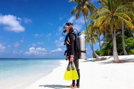 scuba diver sanding on sunny beach with palm trees